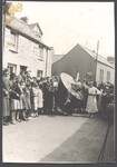 A hobby horse, melodeon player and Betty standing in the street surronded by onlookers