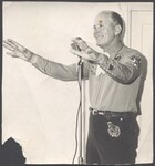 Ray Smith standing at microphone with arms out by Unknown