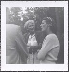 Evelyn K. Wells stands conversing with a man and woman by Unknown