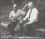 Frank Profitt with banjo and Douglas Kennedy sitting on a log