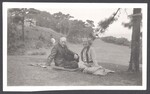 A man and woman sitting on a blanket on a grassy lawn