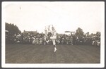 Two Morris dancers performing on a lawn in front of a large crowd